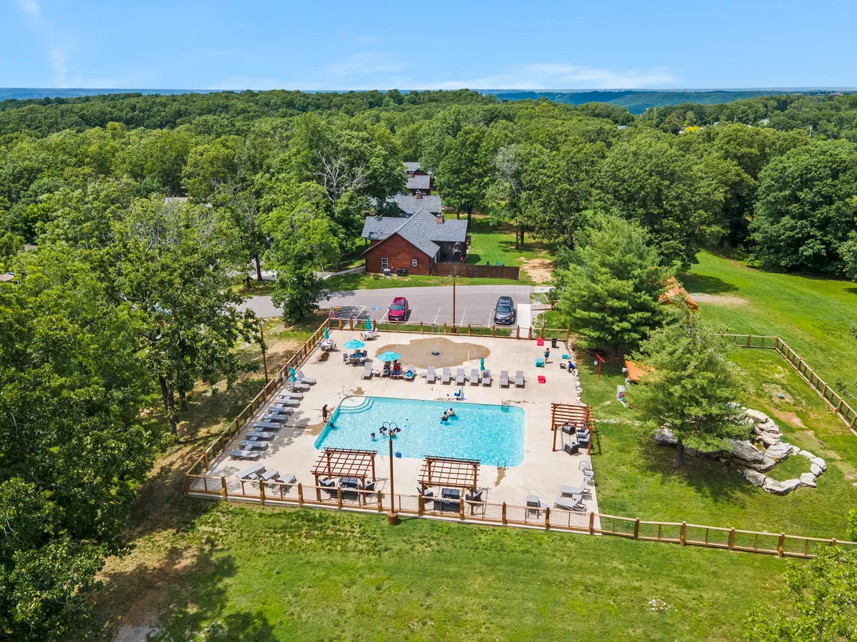A vibrant exterior scene featuring a large swimming pool surrounded by lounge chairs and cabana structures, set amidst green grass and mature trees. Families can be seen enjoying swimming, sunbathing, and socializing, all within a relaxed and family-friendly atmosphere that echoes the fun and leisure described in the section.