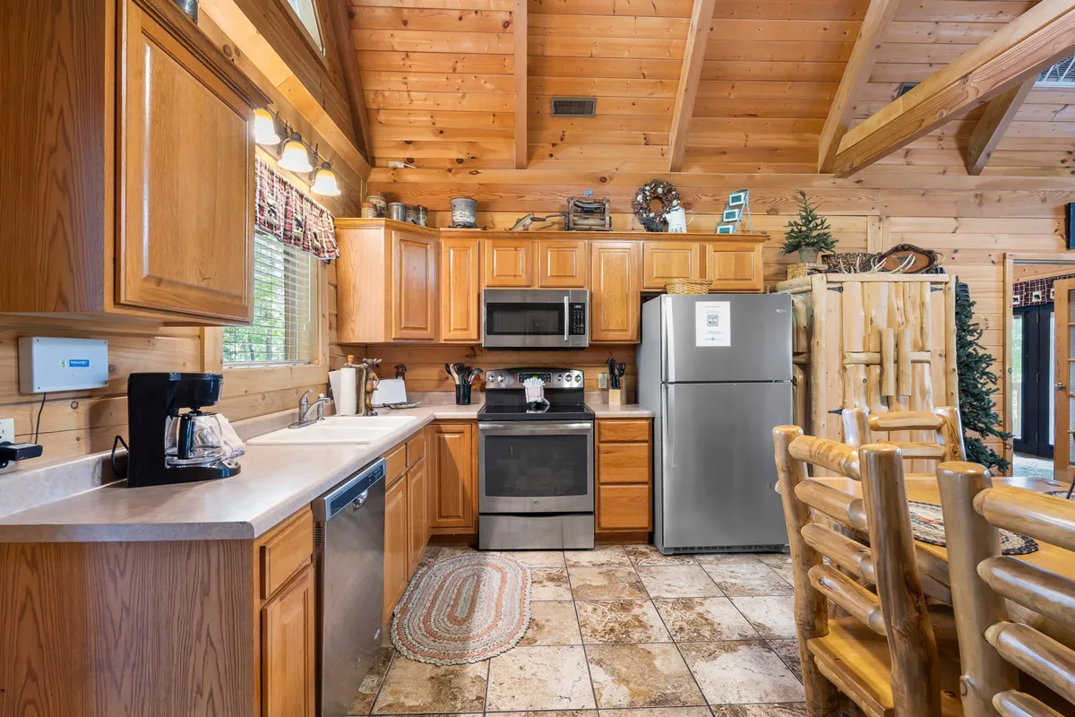 This image focuses on the kitchen area, with warm wooden cabinetry, stainless steel appliances, and a log-style dining set. Natural light streams through windows, illuminating a space perfect for both meal prep and gathering.