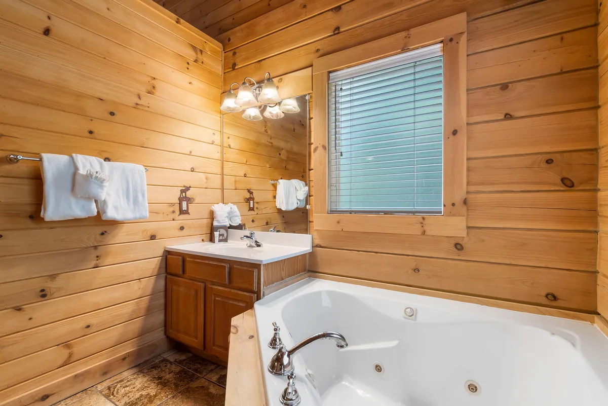 A spa-like master bathroom with a large whirlpool bathtub, double sink vanity, window with blinds, and wood-paneled walls. The ambiance is tranquil and luxurious, perfect for relaxation and unwinding after a day of adventure.
