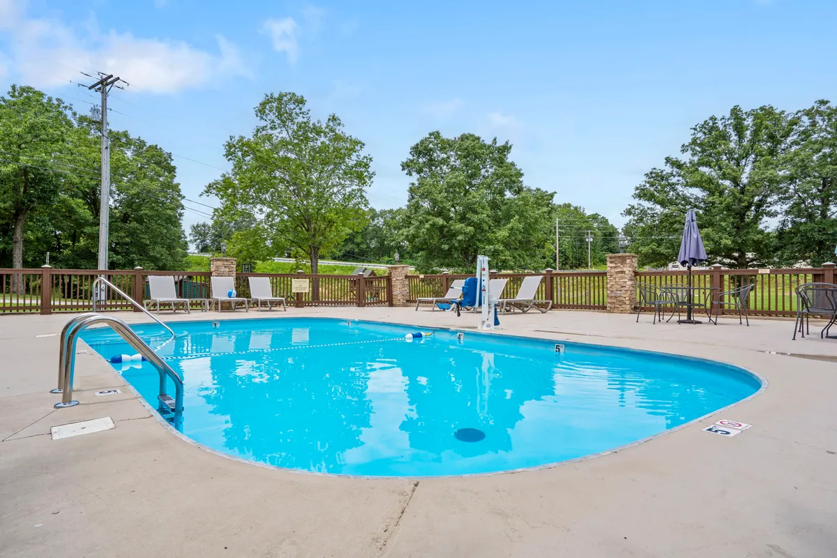 An inviting outdoor swimming pool is surrounded by comfortable lounge chairs and lush greenery. The setting is ideal for swimming, sunbathing, and spending time together, catering to all ages with ample space for both activity and relaxation.