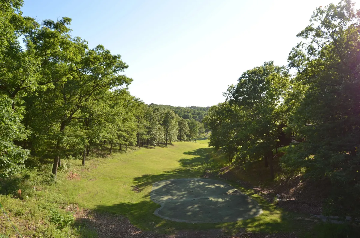 A serene view of a lush green landscape with a manicured golf green in the foreground, surrounded by trees and bathed in gentle sunlight. This image captures the tranquil beauty of the area and alludes to the world-class golf experiences available close by, as mentioned in the section.