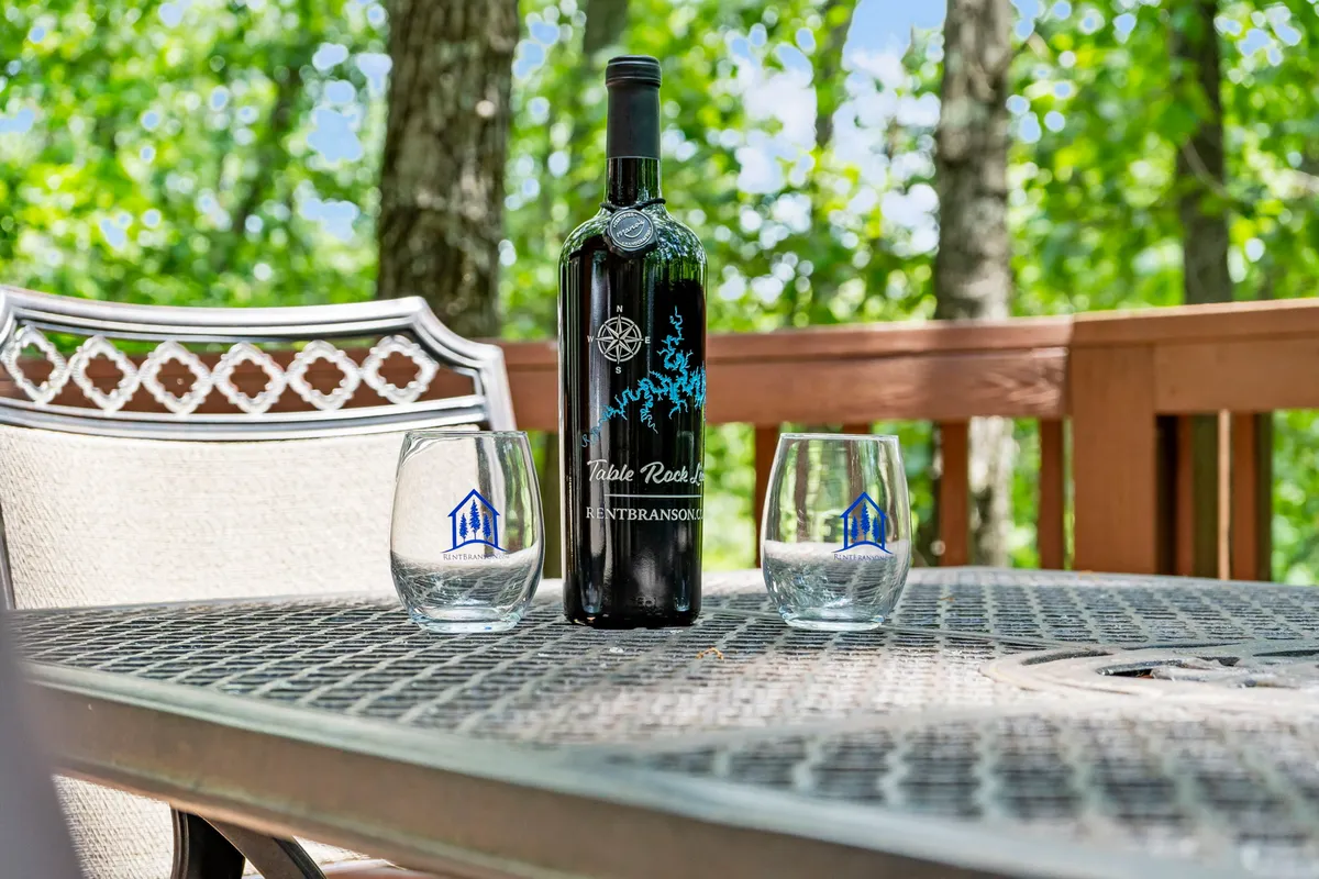 A wine bottle and two glasses set outdoors against a natural backdrop, suggesting a celebratory or intimate moment. The setting highlights sunset views and the pleasure of sharing drinks in a peaceful environment.
