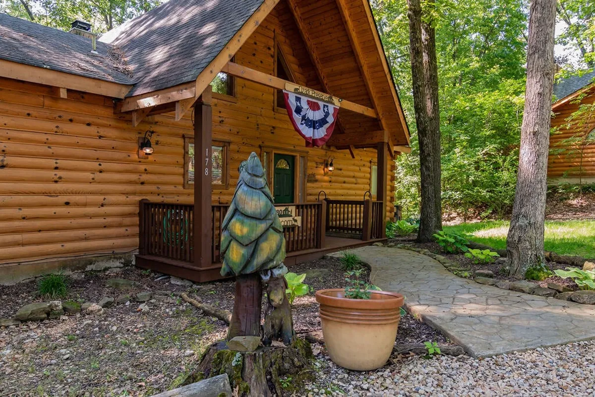 Charming log cabin architecture with a welcoming porch adorned with decorative elements and a unique wooden sculpture. The porch overlooks surrounding trees, setting a cozy and inviting scene for relaxation and wildlife watching.